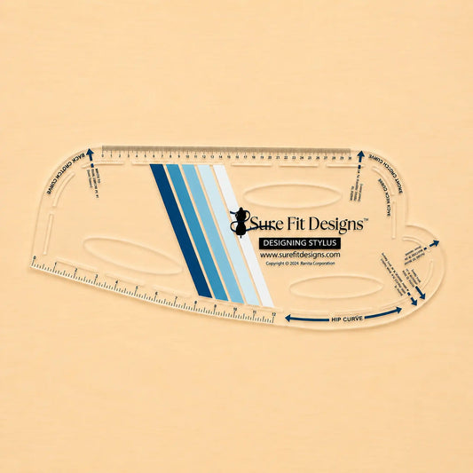 A Sure Fit Designs Designing Stylus quilting ruler, shown from a top-down view on a solid beige background. The clear plastic ruler features blue and light blue striped accents, black printed text, and measurement markings.