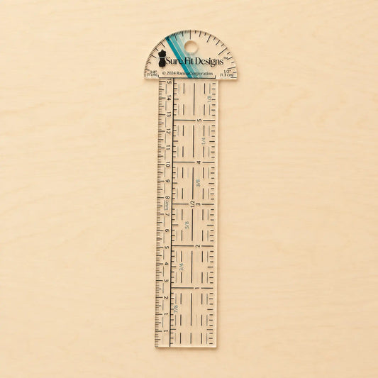 A clear acrylic ruler with a semi-circular protractor top, featuring black measurement markings and the Sure-It Designs logo, displayed vertically on a light wood background.