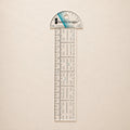 A clear acrylic ruler and protractor set by Sure Fit Designs, featuring black measurement markings and a blue accent stripe on the protractor cap, displayed on a light beige textured background.