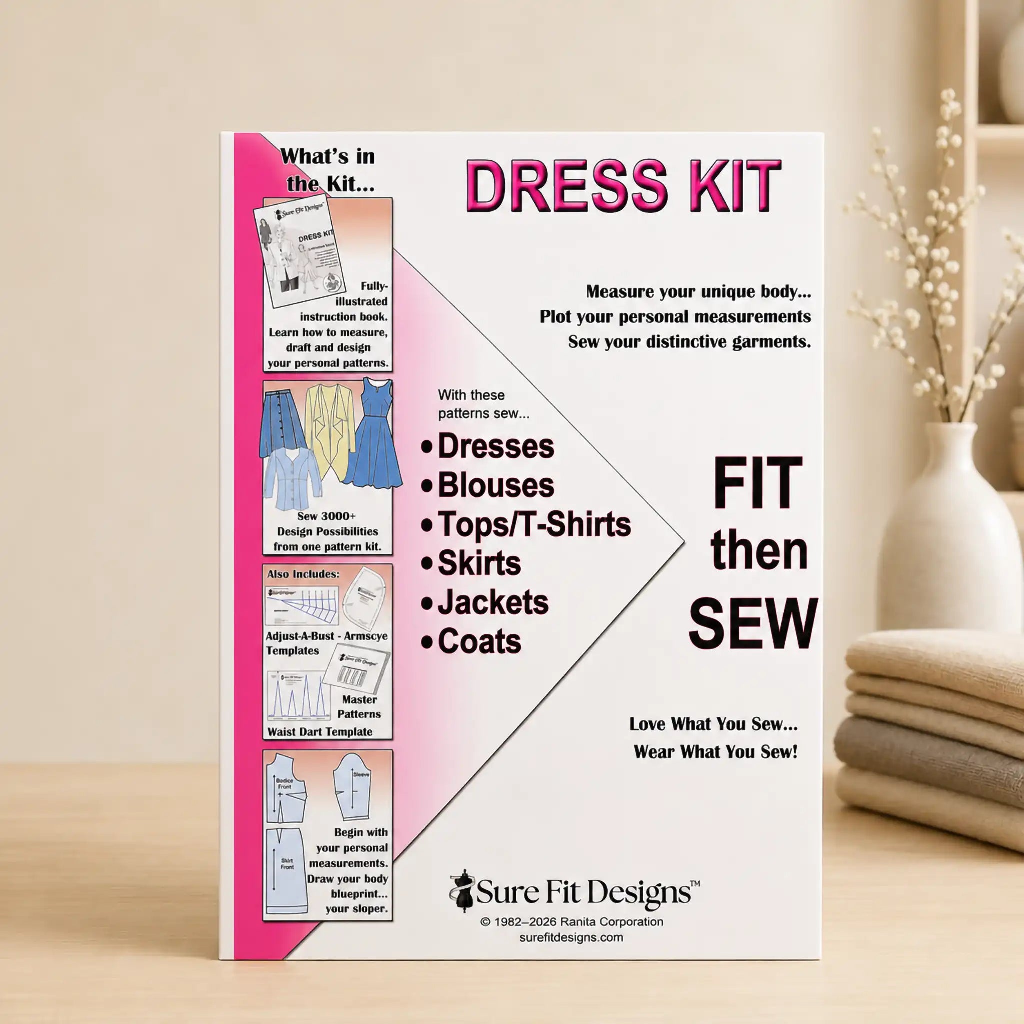 A 'Dress Kit' fit-and-sew instruction card from Sure Fit Designs, displayed upright on a light wooden surface next to a white ceramic vase with dried stems.