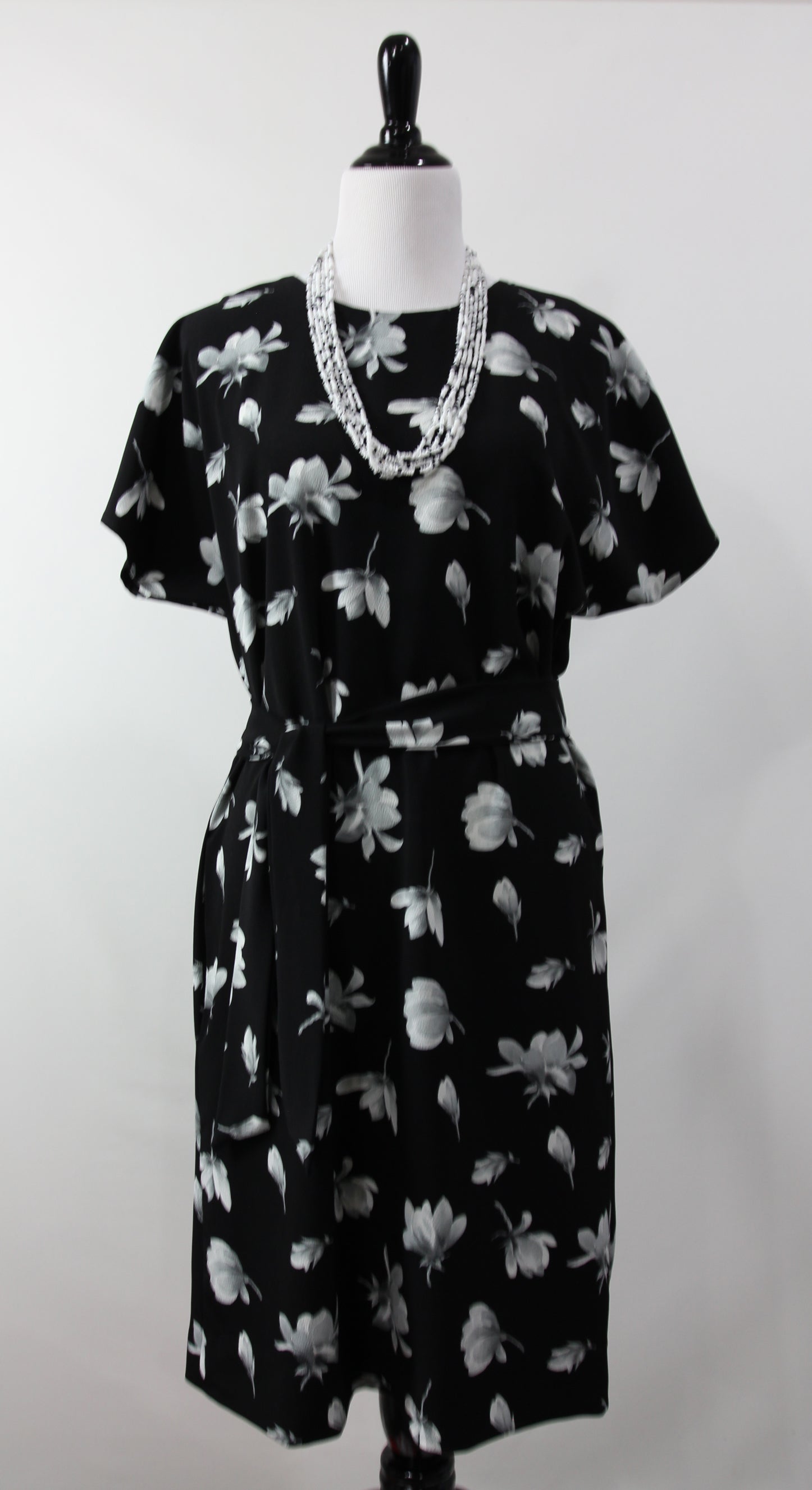 Black dress with white floral pattern on a mannequin against a white background