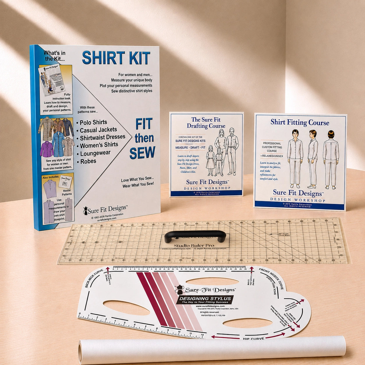 Sure Fit Designers shirt fitting kit displayed on a beige surface with warm sunlight shadows. The kit includes a main instruction booklet, three smaller course/booklet covers, a clear gridded cutting mat, a black rotary cutter, a white arched template, and a white roll of paper.
