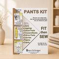 A 'Pants Kit' instruction booklet by Sure Fit Designs stands upright on a light wooden surface. The booklet has a white and beige cover with black and brown text, detailing how to measure and sew pants.