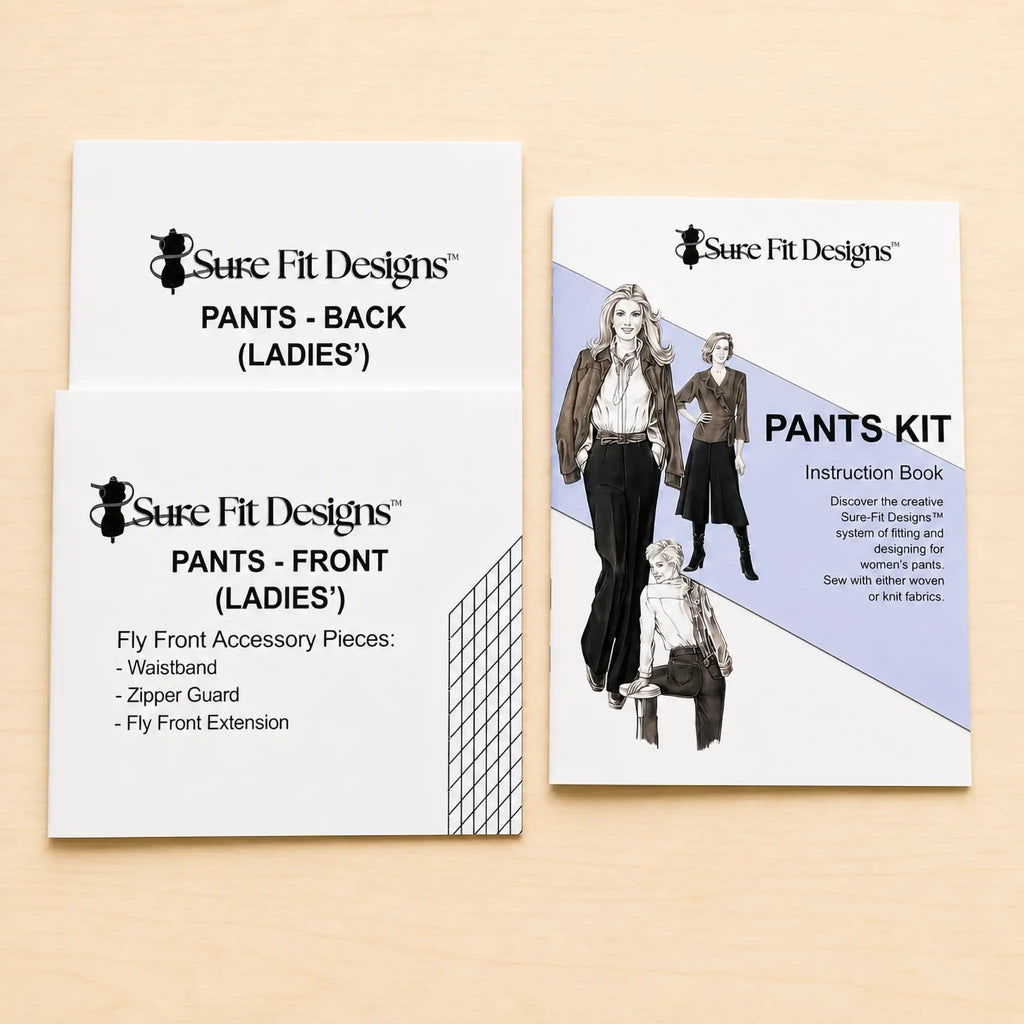 Three Sure Fit Designs sewing kit components for making women's pants laid out on a light wood surface: two white paper pieces labeled 'PANTS - FRONT (LADIES')' and 'PANTS - BACK (LADIES)' plus one instruction book titled 'PANTS KIT'.