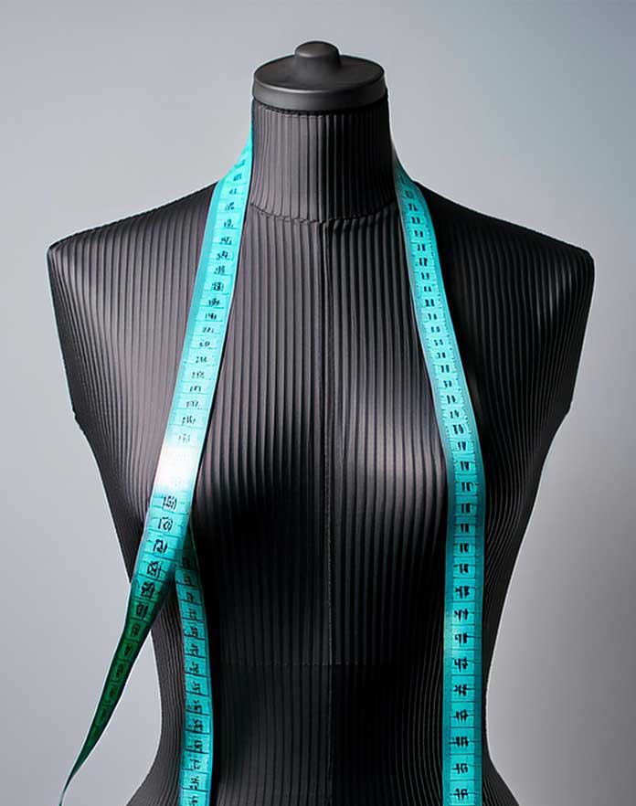 Mannequin torso with a blue measuring tape draped over it on a gray background