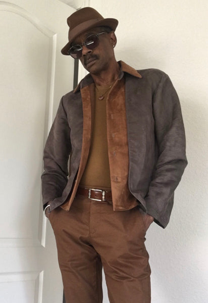 Man wearing a brown jacket, shirt, pants, and hat against a white background